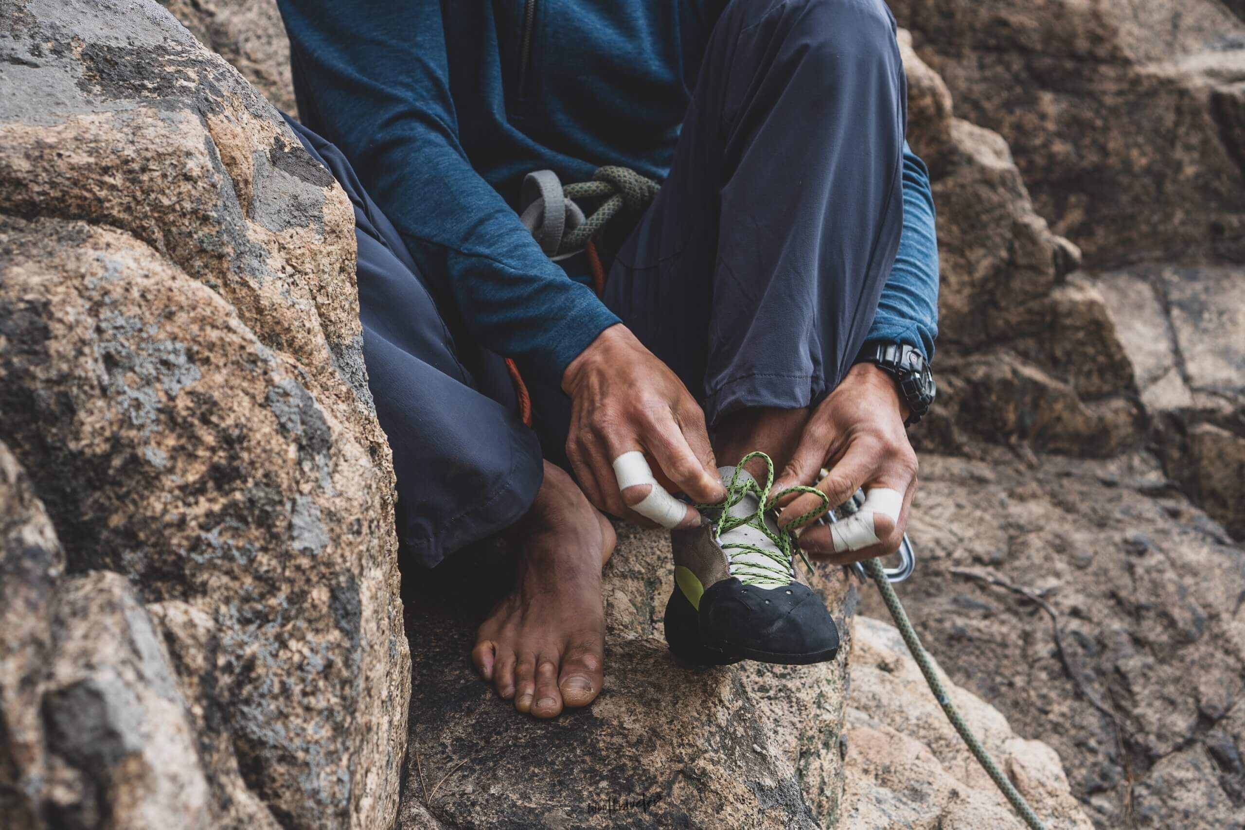 man tying climbing shoes while sitting on rock